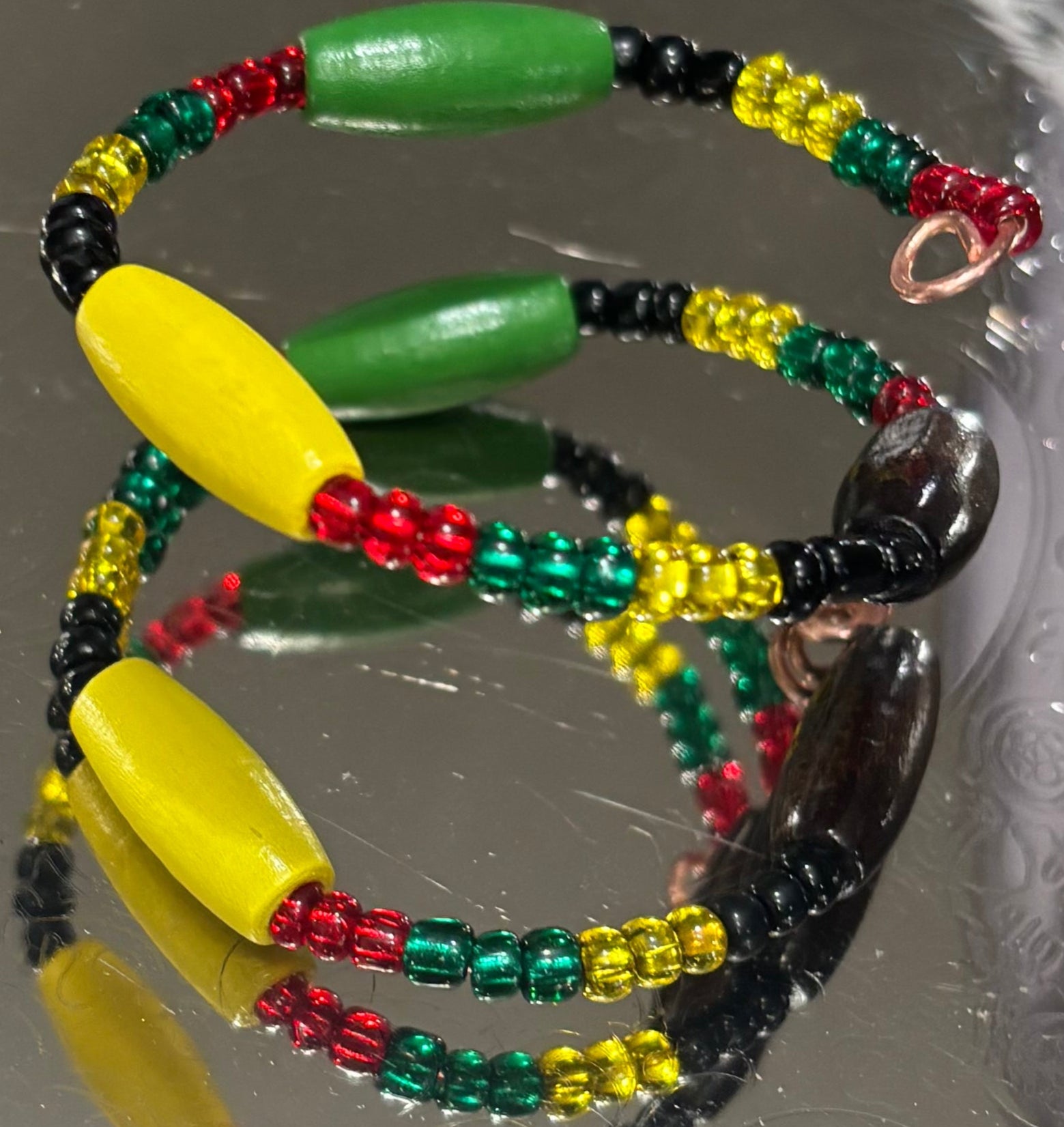 Colorful beaded bracelet with green, yellow, red, and black beads on a reflective surface.